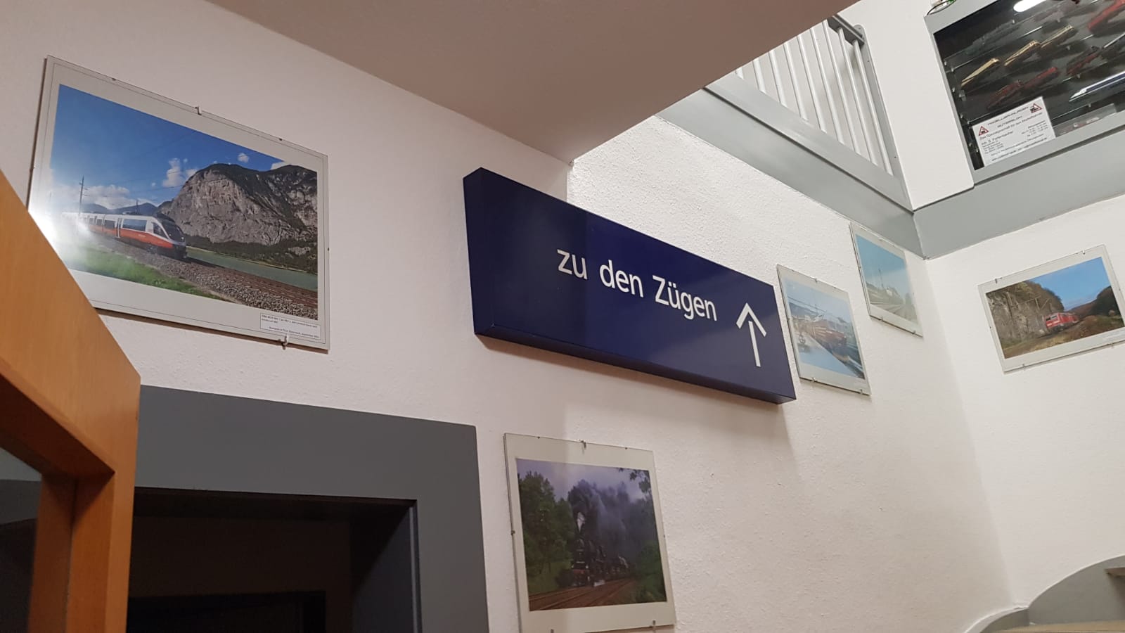 Treppenaufgang im Clubhaus mit Schild „Zu den Zügen“ und Eisenbahnbildern