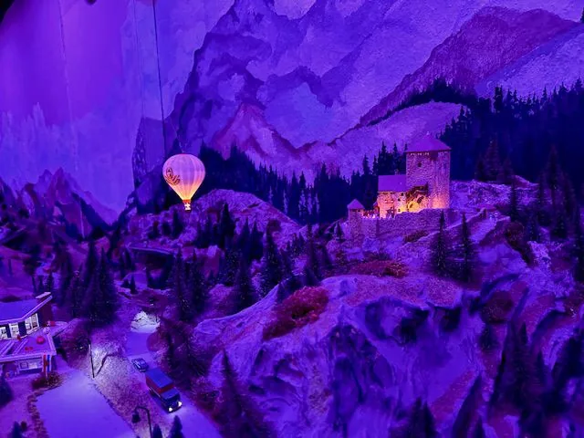 Coburg bei Nacht im blauen Raumlicht, darüber ein leuchtender Heißluftballon vor der Bergkulisse